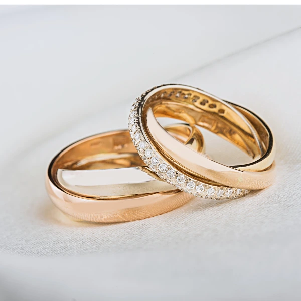 Three gold wedding rings with diamonds on a white surface.