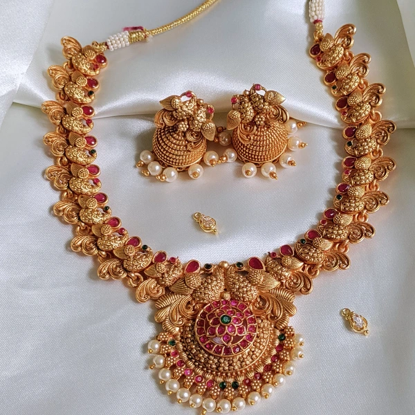 "Gold-toned traditional Indian jewelry set with necklace, earrings, and mang tikka, embellished with pearls and gems. Perfect for online artificial jewellery shopping, offering exquisite designs at affordable prices."
