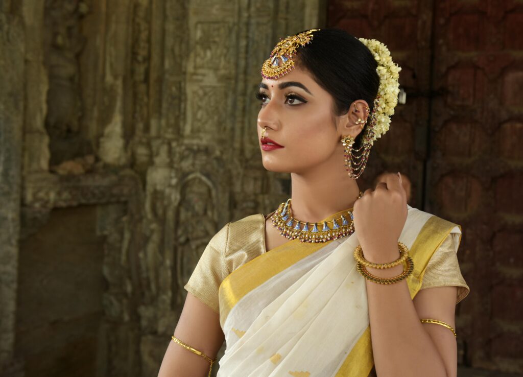 Woman in traditional Indian saree,wearing beautiful floral garland and finest artificial jewellery online, against an ancient carved stone backdrop.