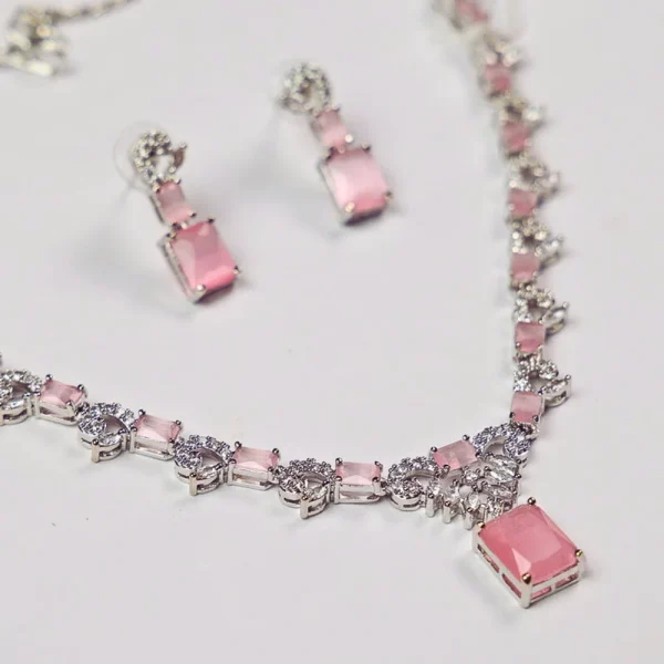 Silver necklace with pink gemstones and matching earrings displayed on a white background.