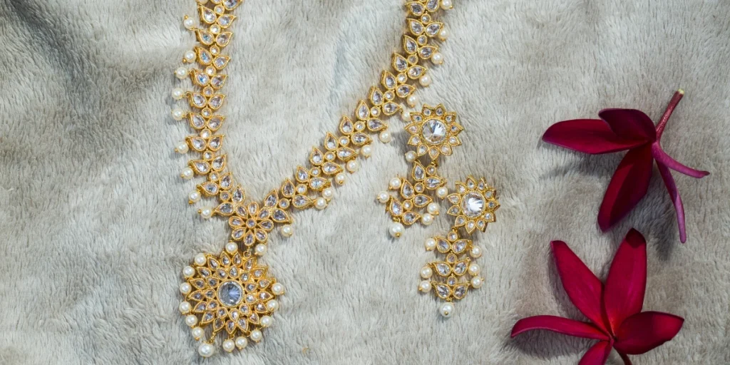 Gold ornate polki jewellery with pearls on a soft background, accompanied by red leaves.