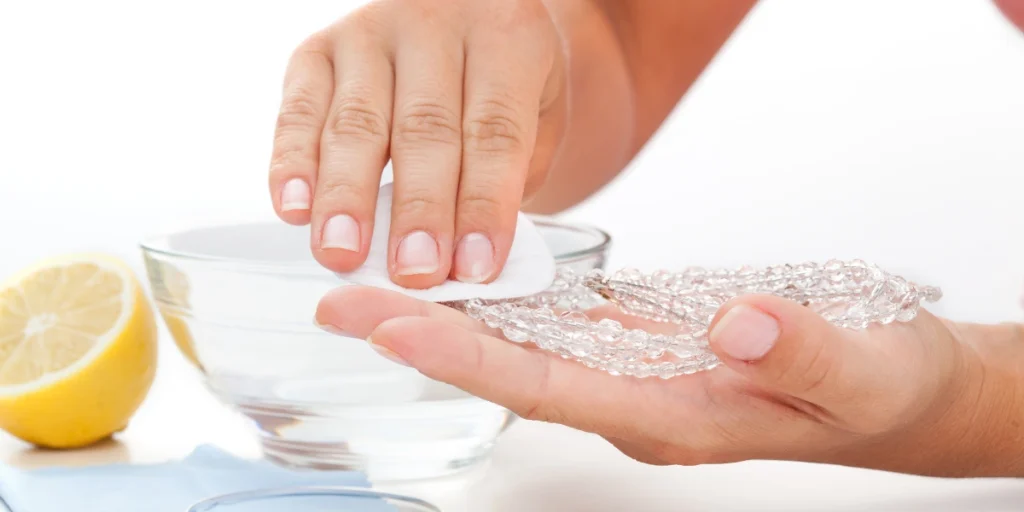 A person showing how to clean oxidised jewellery in a bowl of water with lemon, with a focus on their hands.