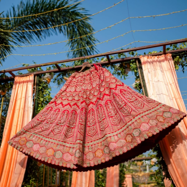 bridal lehenga with jewellery hanging against a blue sky, surrounded by greenery and soft, flowing fabric drapes.